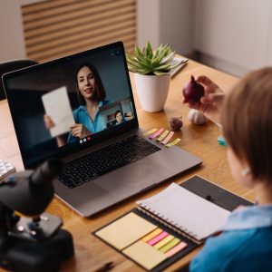 A Preteen boy uses a laptop to make a video call with his teacher. The Screen shows an online lecture with a teacher explaining the subject from class.