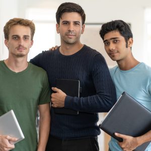 United mix raced team of students United mix raced team of students. Portrait of three young men in casual wear standing in classroom and hugging each other. Corporate education concept.
